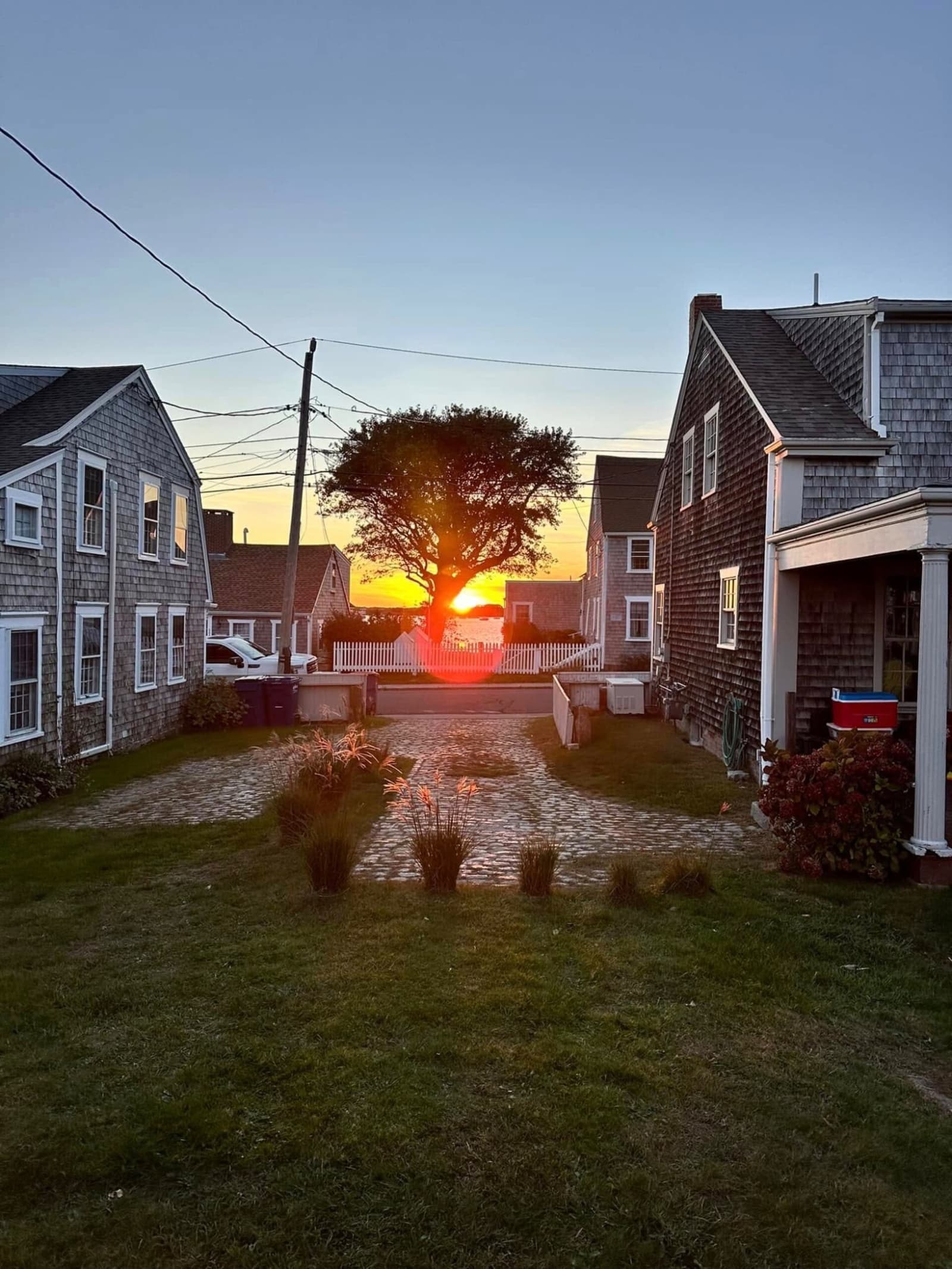 Sun setting through the gap between shingled houses, cobblestones glowing at Westport Point