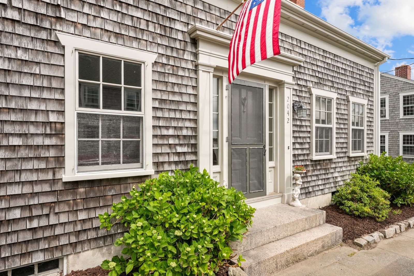 Front door of 2042 Main Road with granite steps, American flag, and address marker
